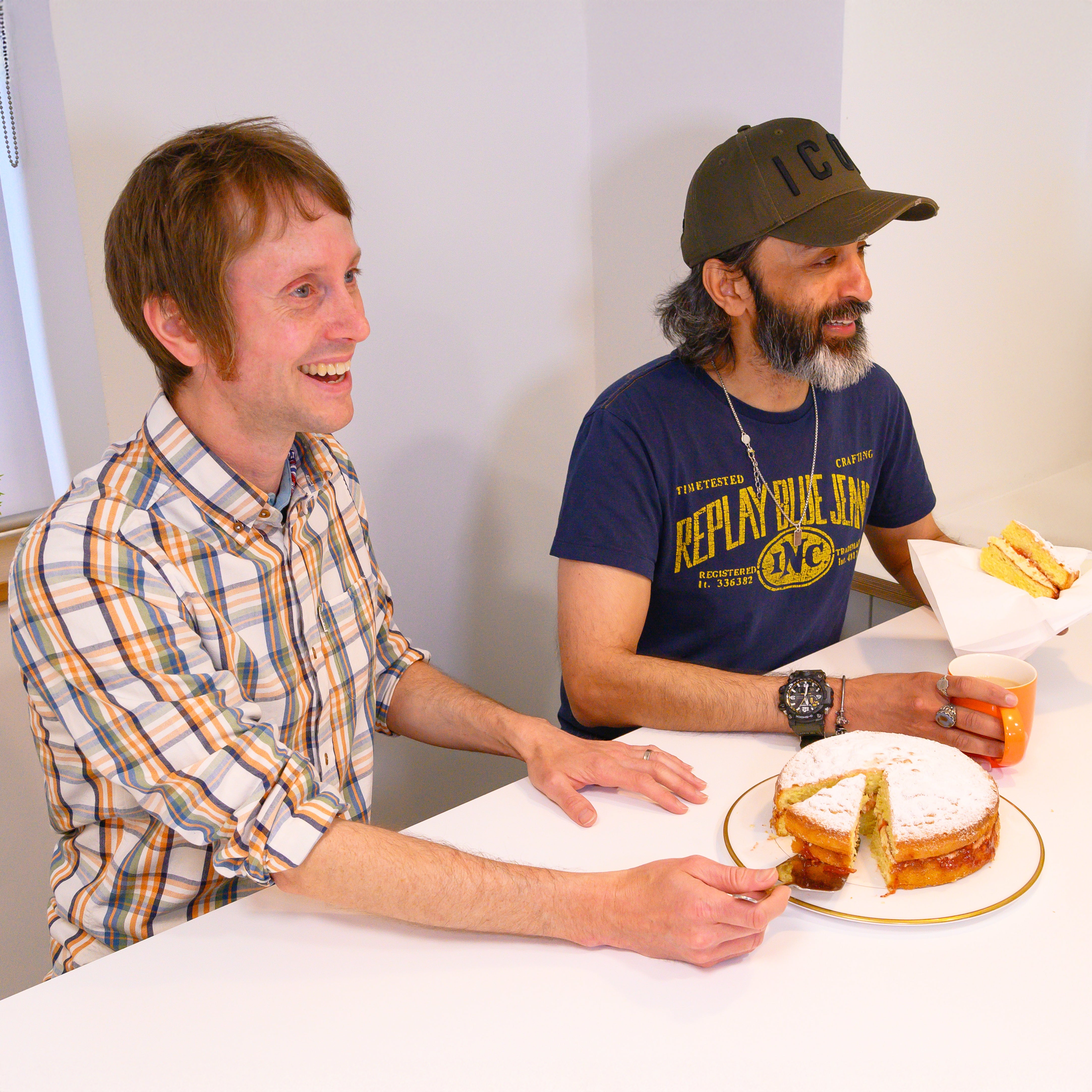 Two men sitting at a table, sharing cake and engaging in conversation